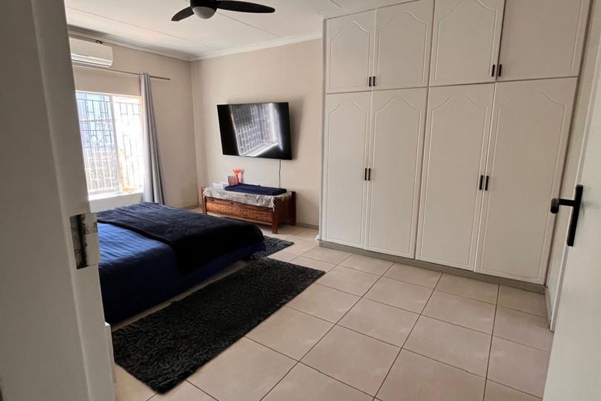 Spacious bedroom featuring neutral tiled flooring, extensive built-in cabinetry, a ceiling fan, and a wall-mounted air conditioning unit.