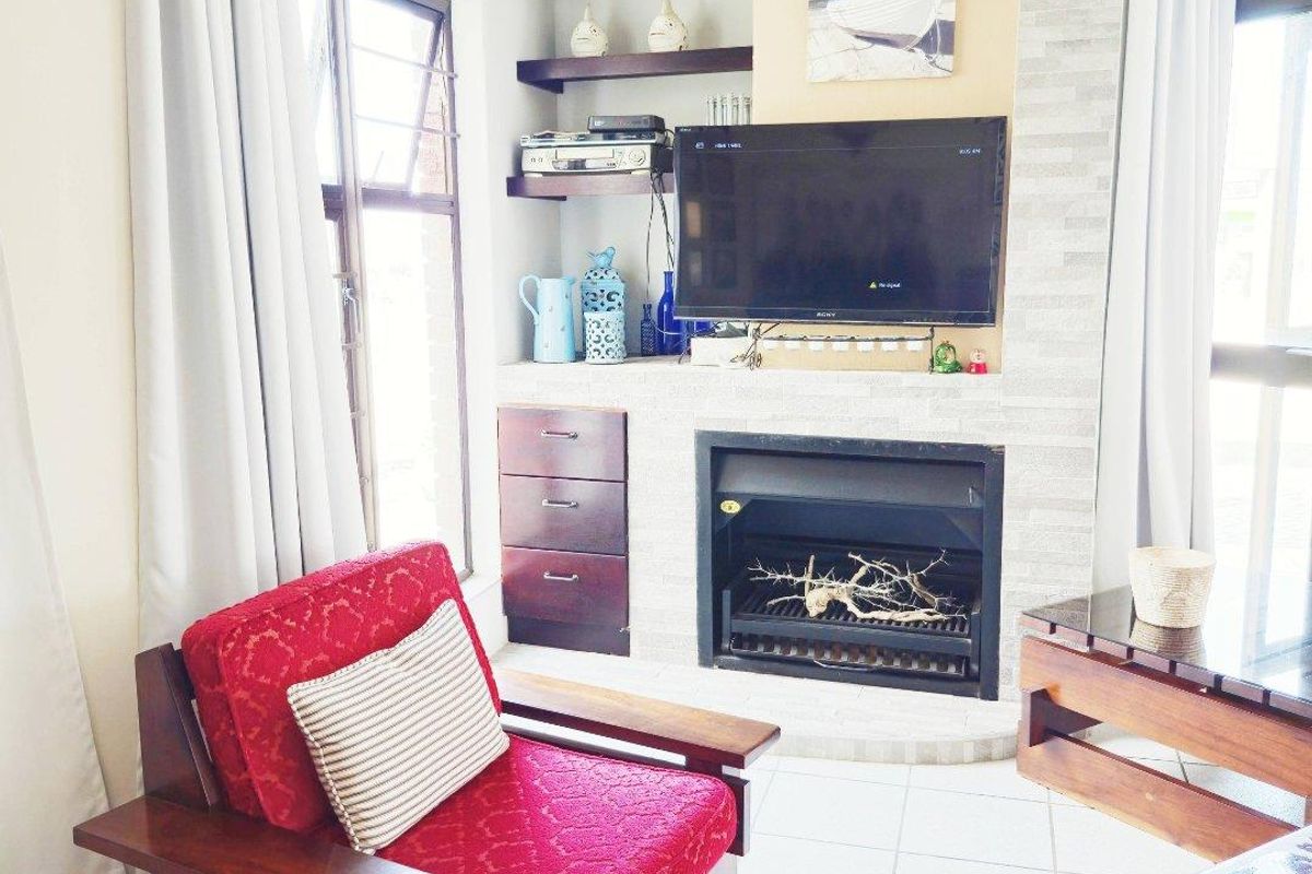 A cozy living room featuring a built-in fireplace with stone cladding, integrated shelving, and tiled flooring, creating a warm and functional living space.