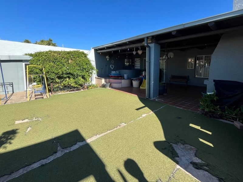 Rear garden area featuring a covered patio with tiled flooring and an artificial lawn that requires maintenance.