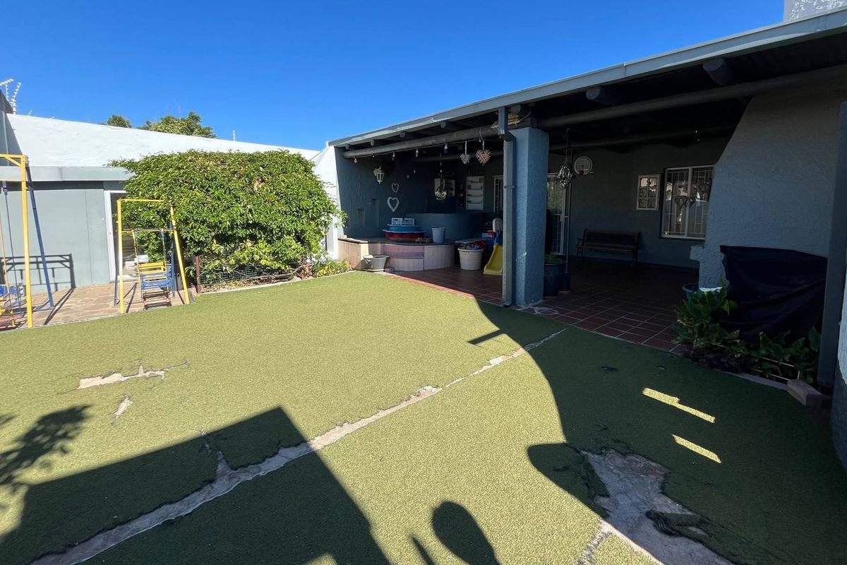 Rear garden area featuring a covered patio with tiled flooring and an artificial lawn that requires maintenance.