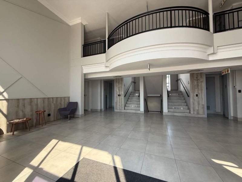 Spacious office building entrance lobby featuring a mezzanine level, modern tiled flooring, and a central staircase with metal handrails.
