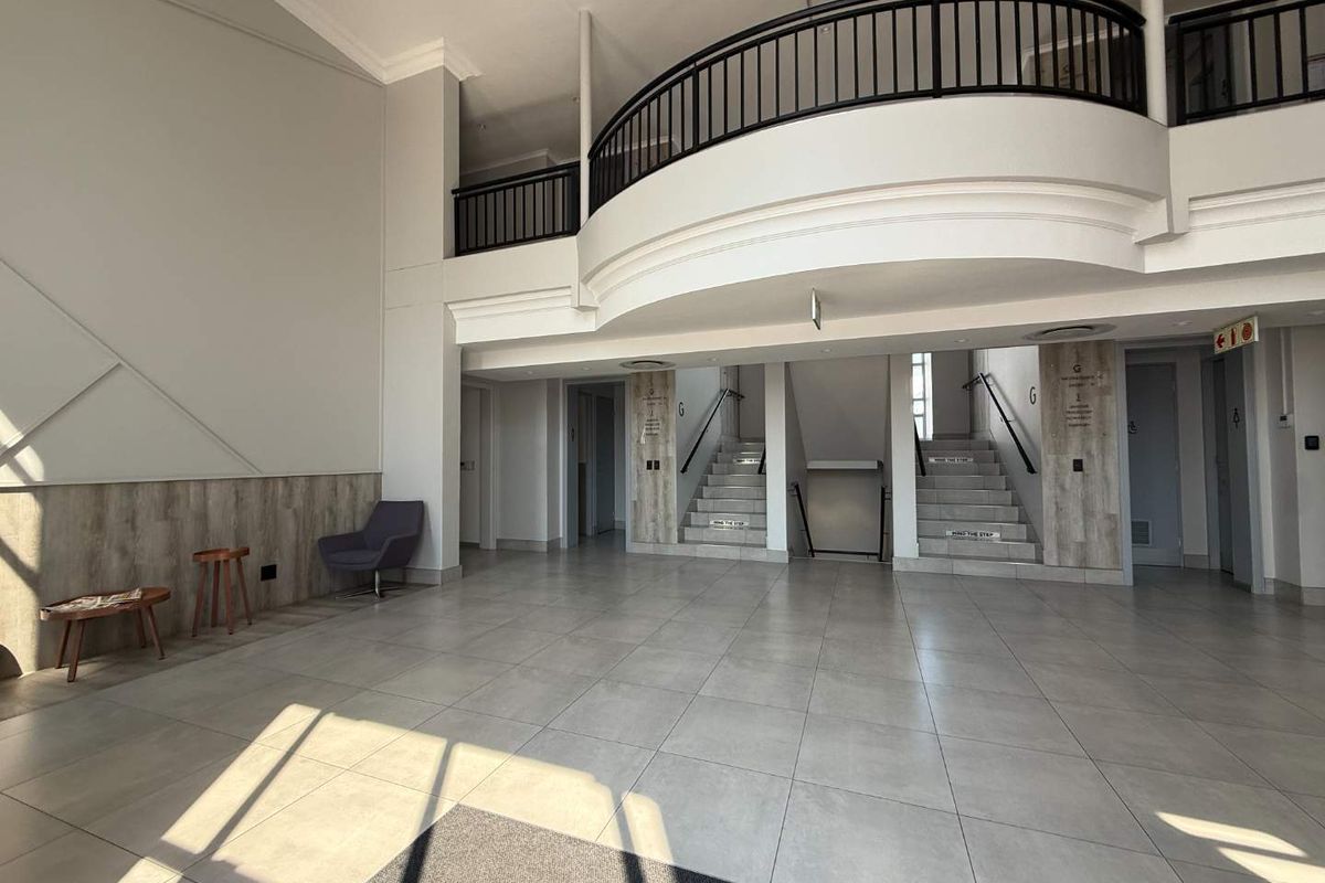 Spacious office building entrance lobby featuring a mezzanine level, modern tiled flooring, and a central staircase with metal handrails.