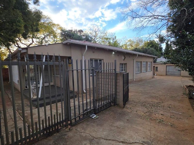 Front exterior view of a single-story house featuring a metal security gate, concrete driveway, and a detached garage.