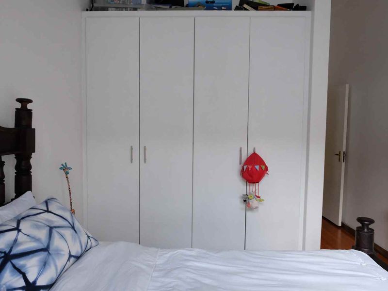 A bedroom featuring a floor-to-ceiling white built-in wardrobe and hardwood flooring.