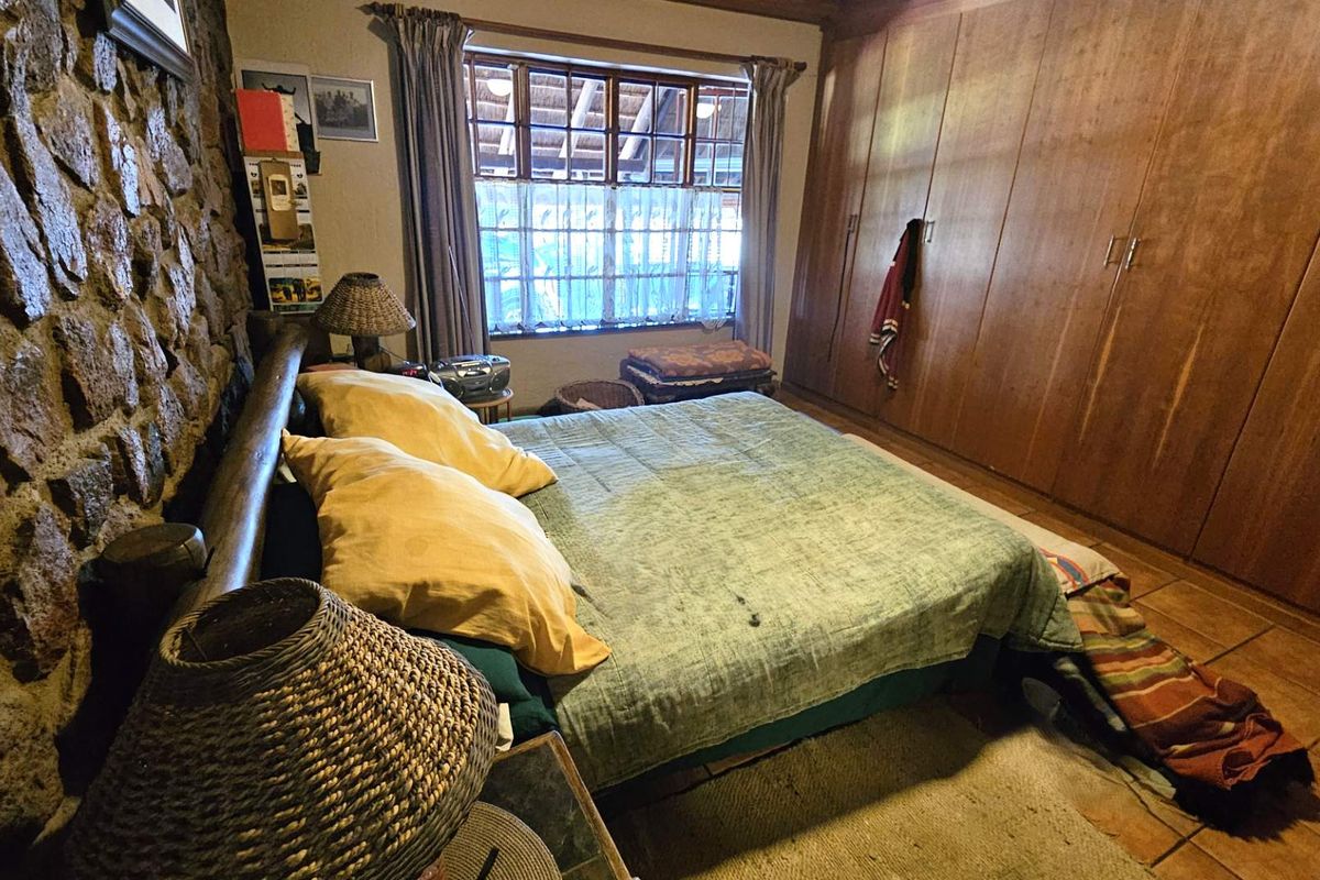 A rustic bedroom featuring a natural stone feature wall, built-in wooden wardrobes, and tiled flooring, offering a warm and textured aesthetic.