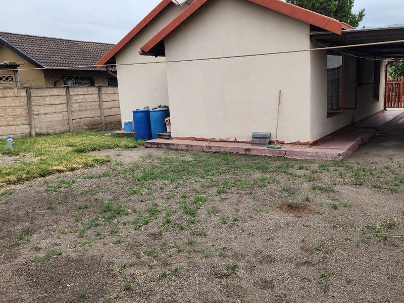 Rear exterior view of the property featuring a concrete boundary wall, a carport structure, and a basic yard area with a concrete apron.