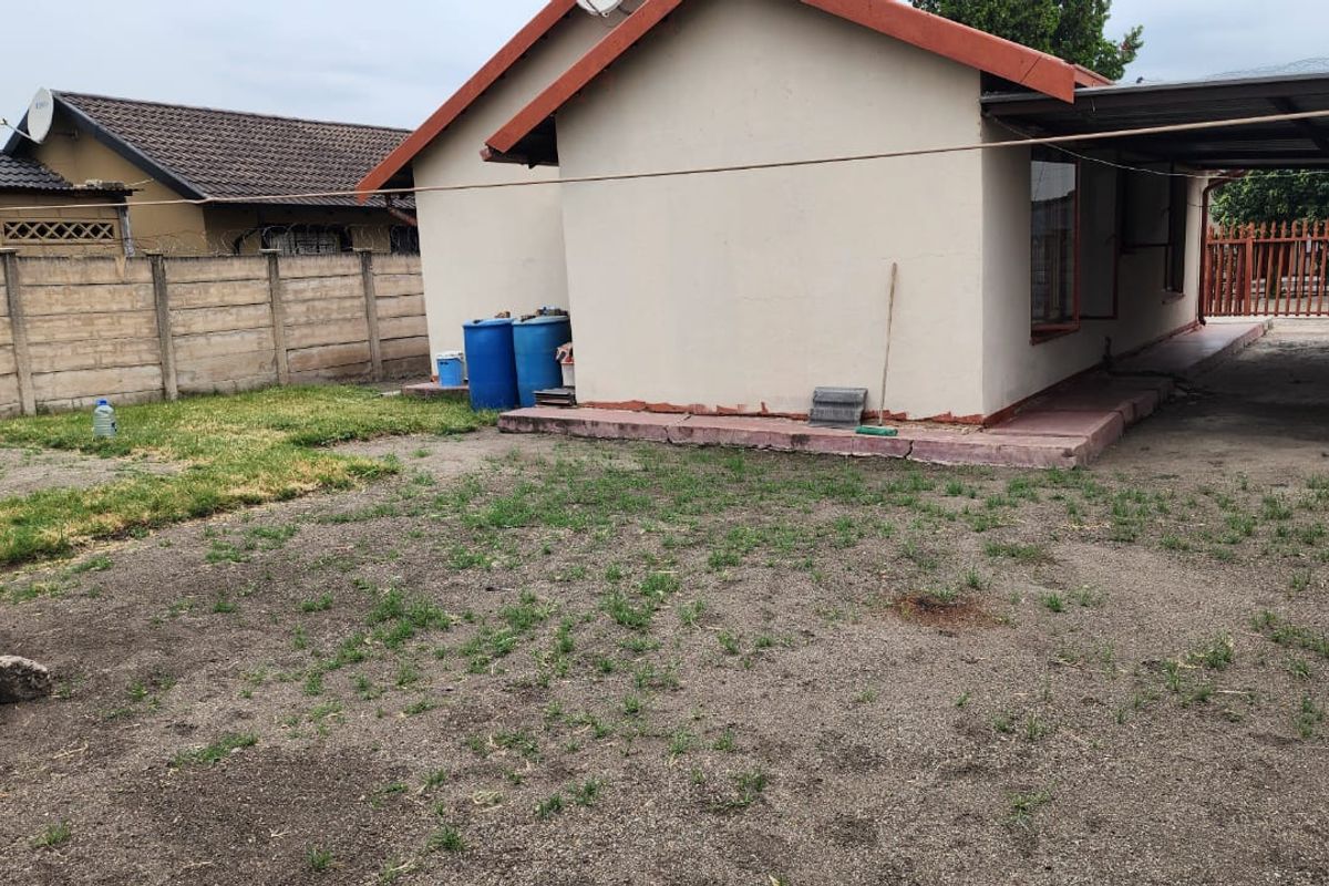 Rear exterior view of the property featuring a concrete boundary wall, a carport structure, and a basic yard area with a concrete apron.