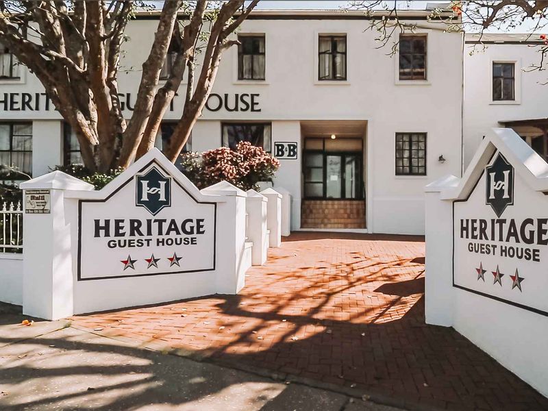 Front exterior view of the Heritage Guest House featuring a brick-paved entrance, masonry boundary walls, and a multi-story building facade.