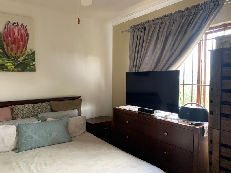 A functional bedroom featuring a ceiling fan, coving, and security bars on the window, providing a comfortable and secure living space.