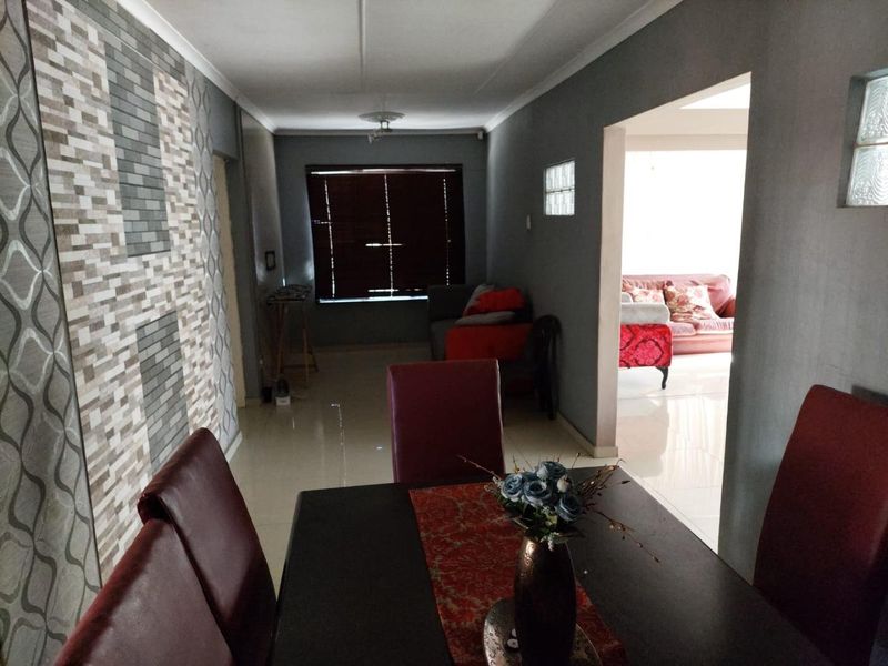 Open plan living and dining area featuring tiled flooring, a decorative feature wall, and a glass block window detail.