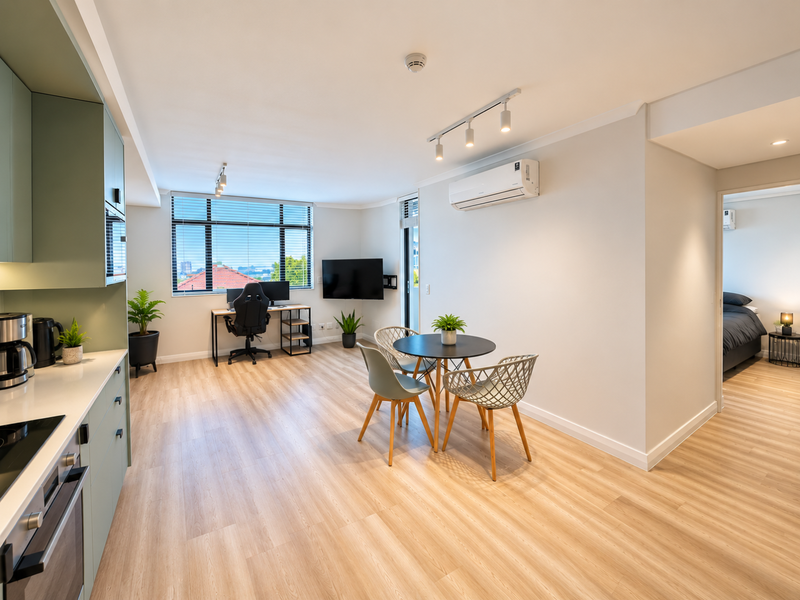 Modern open-plan apartment featuring a sleek kitchen with built-in cabinetry, integrated appliances, and light wood-look flooring, seamlessly flowing into a bright living and dining area.