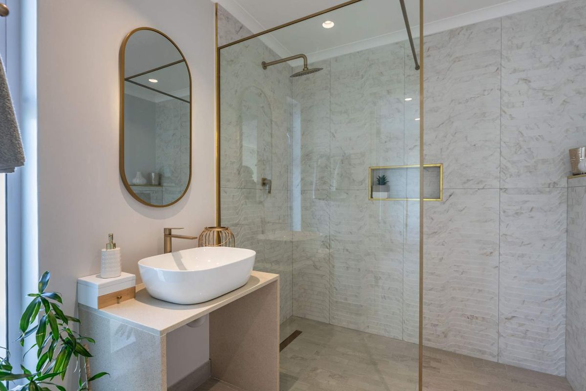 Modern bathroom featuring a walk-in shower with glass screen, marble-look wall tiles, brass fixtures, and a contemporary vessel sink vanity.