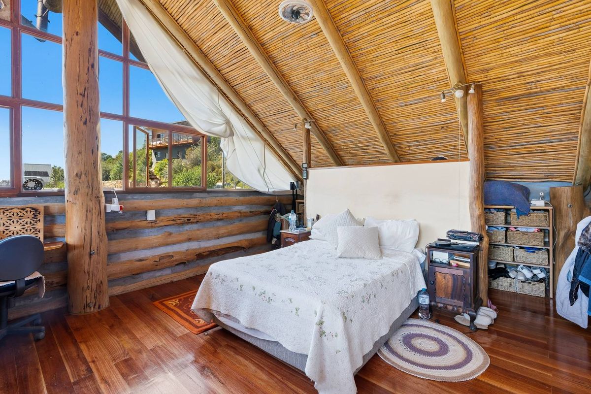A unique bedroom featuring rustic timber log walls, a vaulted bamboo ceiling with exposed rafters, and large windows offering natural light and scenic views.
