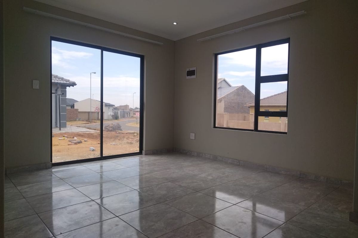 A bright, empty living area featuring modern tiled flooring, large aluminium-framed windows, and a sliding glass door providing natural light and outdoor access.