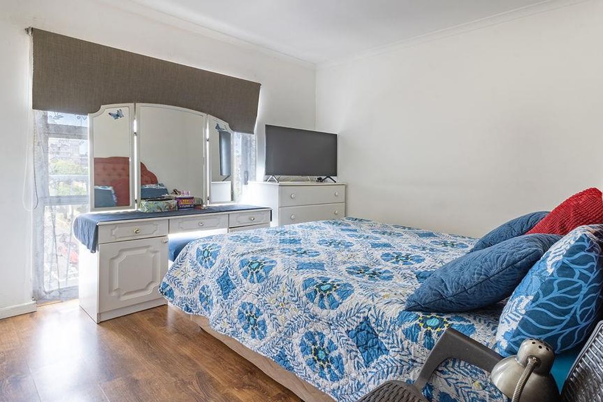 A bedroom featuring laminate flooring, a large window with a roller blind, and coved ceiling detailing.