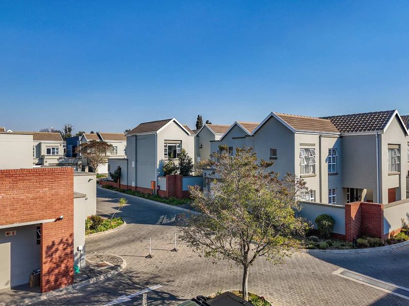 An elevated view of a modern cluster housing complex featuring paved driveways, brick accents, and well-maintained residential facades under a clear blue sky.