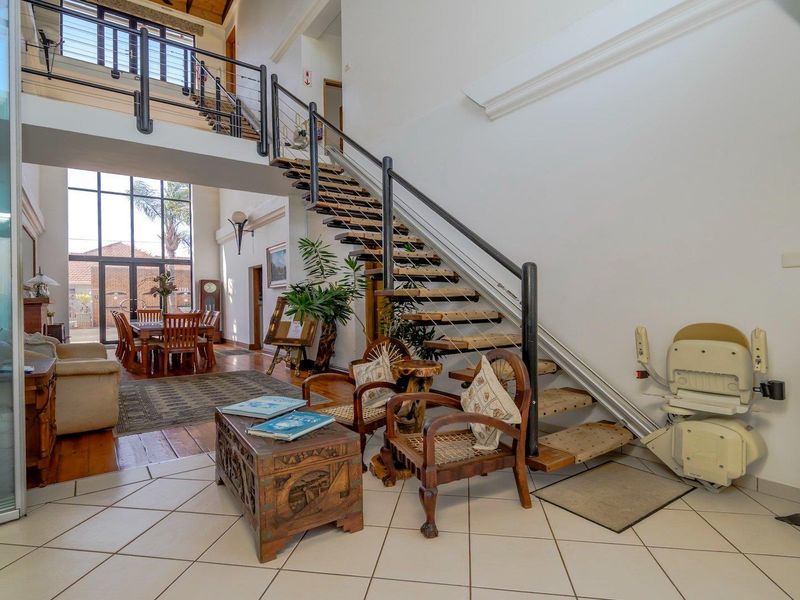Spacious double-volume entrance hall featuring a modern staircase with metal balustrades, a fitted stairlift, and large windows providing ample natural light.