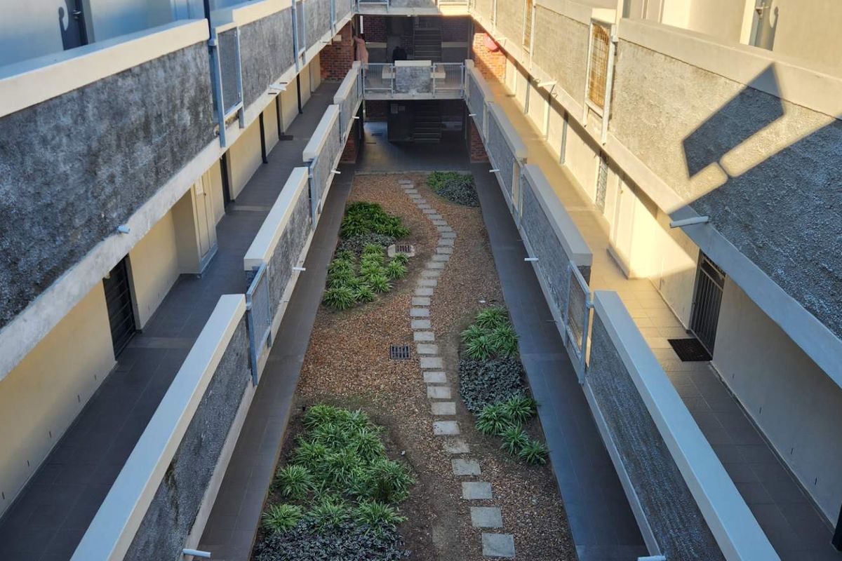 An elevated view of an apartment complex courtyard featuring a central landscaped garden path flanked by walkways and building facades.