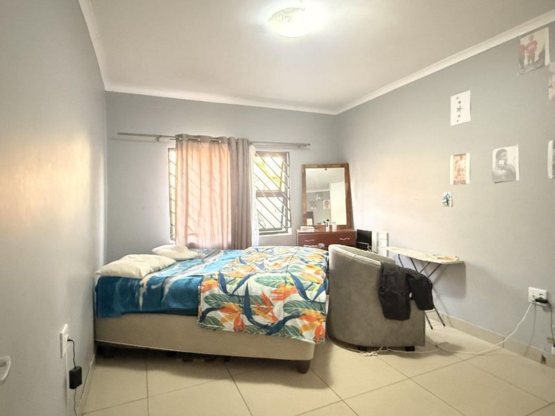 A standard bedroom featuring tiled flooring, security bars on the window, and neutral wall finishes.