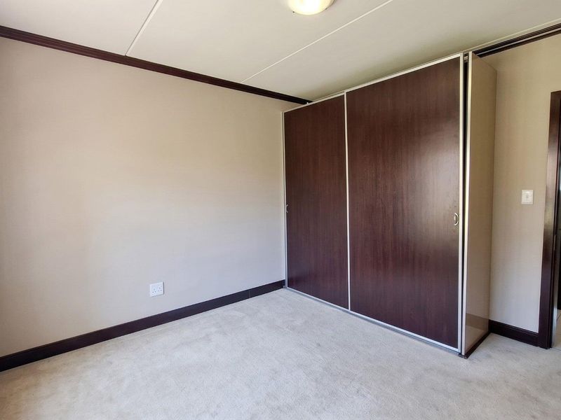A clean, empty bedroom featuring neutral walls, carpeted flooring, and a large built-in wardrobe with dark wood-finish sliding doors.