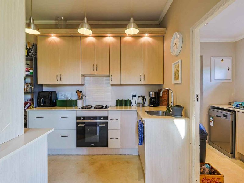 Compact kitchen featuring light wood cabinetry, built-in oven, gas hob, and a separate scullery area with additional counter space.