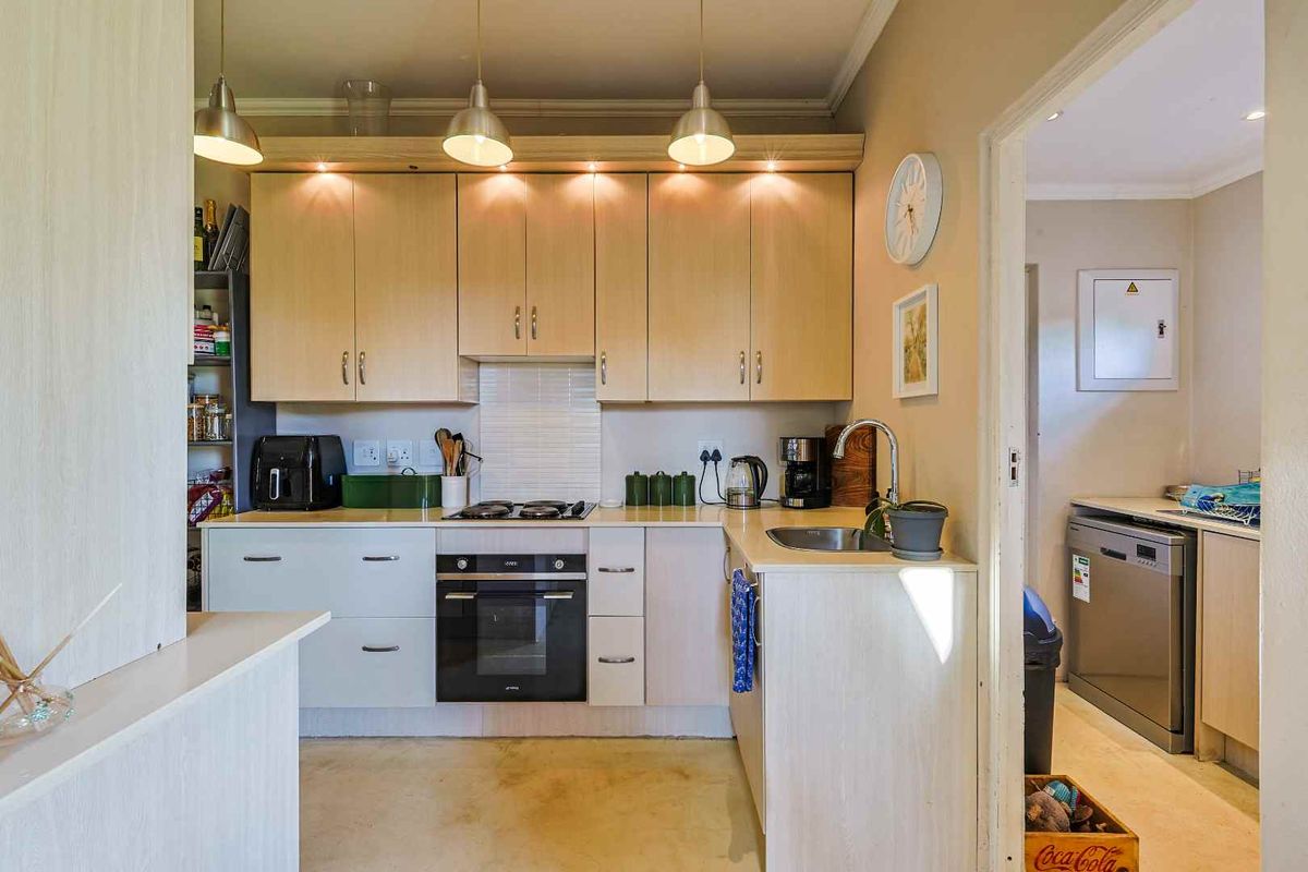 Compact kitchen featuring light wood cabinetry, built-in oven, gas hob, and a separate scullery area with additional counter space.