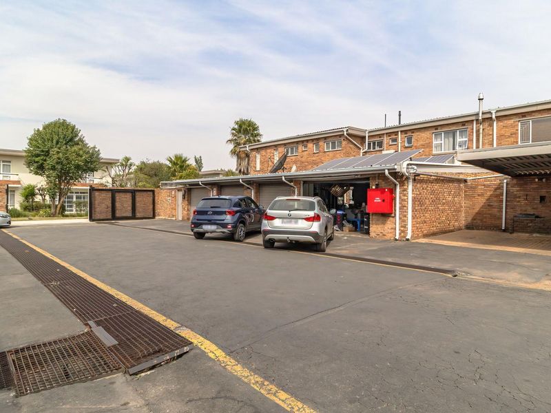 Exterior view of a townhouse complex featuring brick facades, covered parking bays, solar panels, and a paved driveway with integrated drainage.