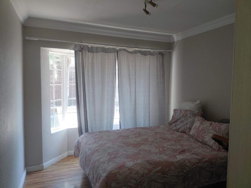 A bedroom featuring laminate flooring, a bay window, and ceiling cornice detailing, providing a functional and well-lit sleeping space.