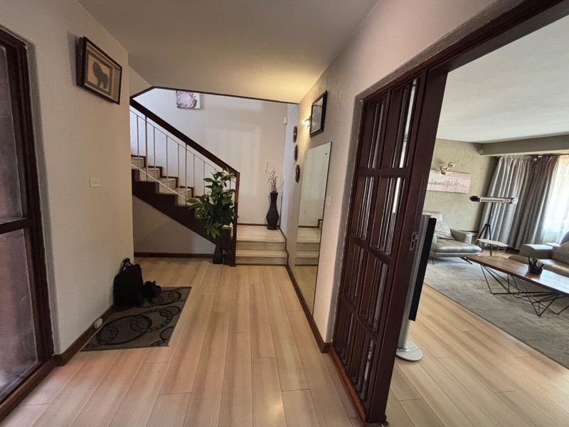 Welcoming entrance hall featuring laminate flooring, a staircase with metal railings, and a timber-framed glass door leading into the main living area.