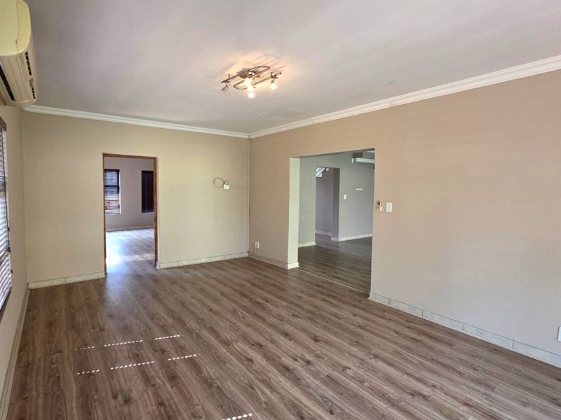 A spacious, empty living room featuring modern laminate flooring, neutral wall tones, and an installed air conditioning unit.