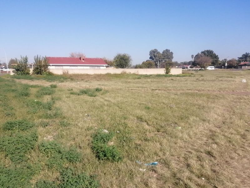 A vacant residential plot of land featuring open grassland and a perimeter boundary wall.