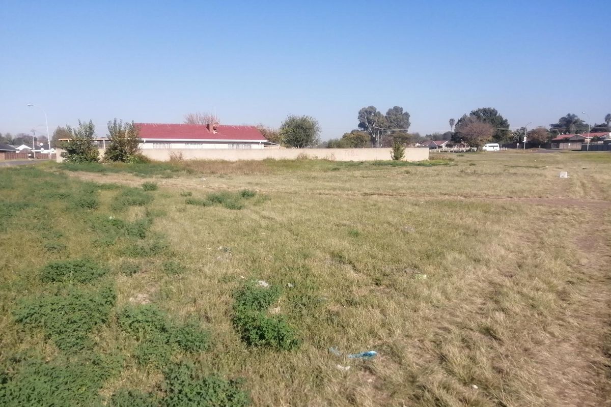 A vacant residential plot of land featuring open grassland and a perimeter boundary wall.