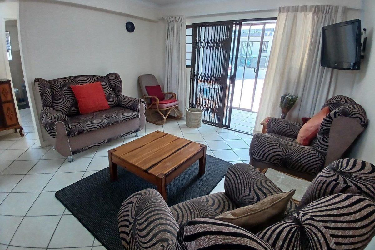 A living room featuring ceramic floor tiles and a sliding glass door with a security gate, providing direct access to an outdoor patio area.