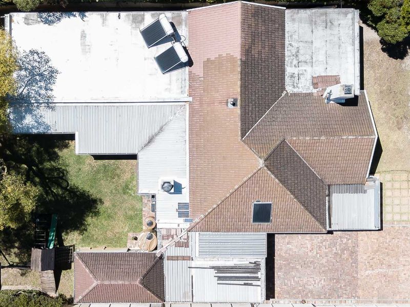 Aerial view of the property showing the roof structure, solar water heating system, paved driveway, and surrounding garden area.