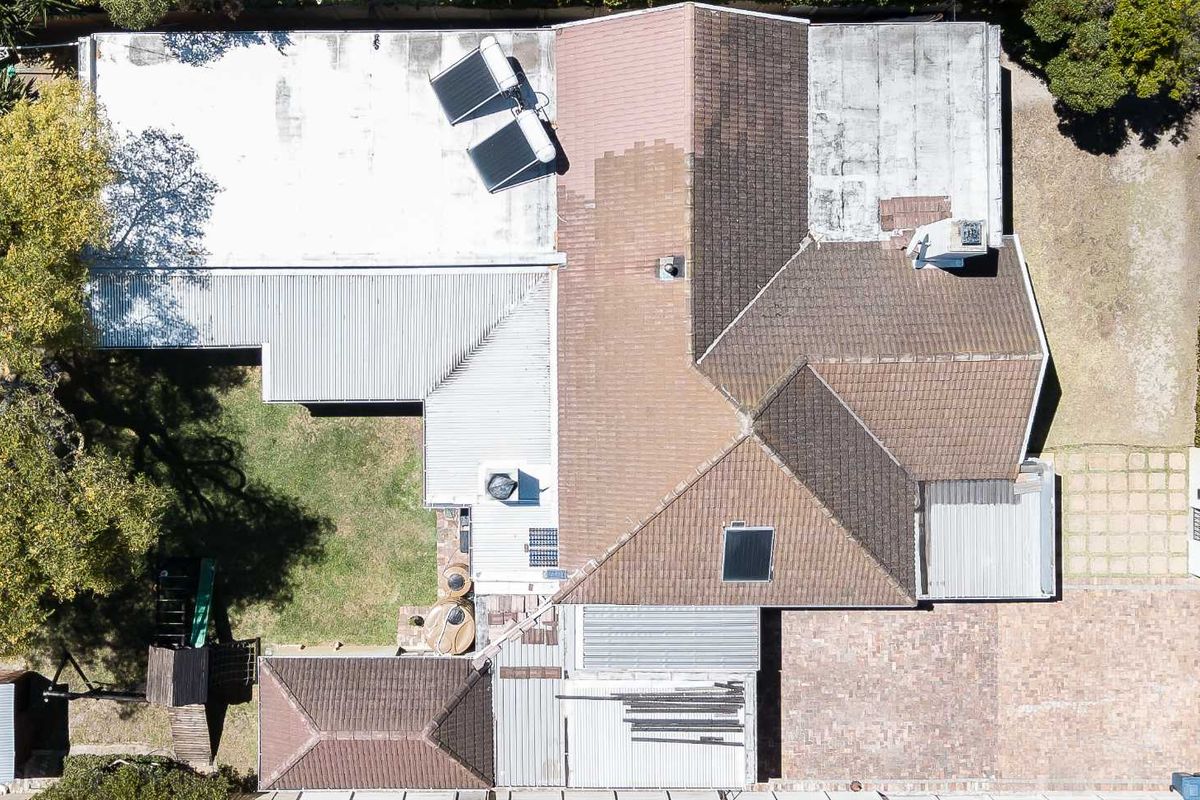 Aerial view of the property showing the roof structure, solar water heating system, paved driveway, and surrounding garden area.