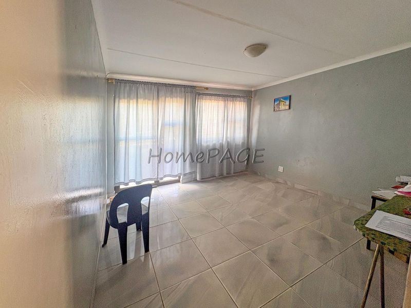 A bright, empty living room featuring neutral tiled flooring and a large sliding glass door providing natural light.
