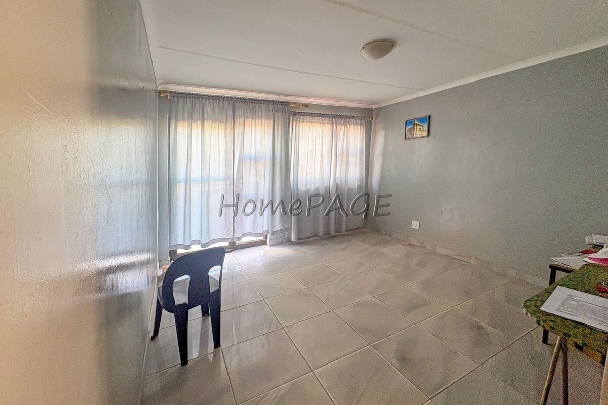 A bright, empty living room featuring neutral tiled flooring and a large sliding glass door providing natural light.