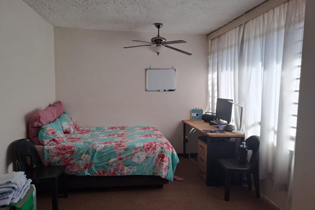 A functional bedroom featuring a ceiling fan, large window with curtains, and carpeted flooring, providing a comfortable and well-lit living space.