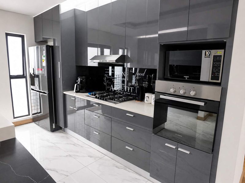 Modern kitchen featuring high-gloss grey cabinetry, stone countertops, integrated appliances including a gas hob, oven, and microwave, complemented by marble-look floor tiles.