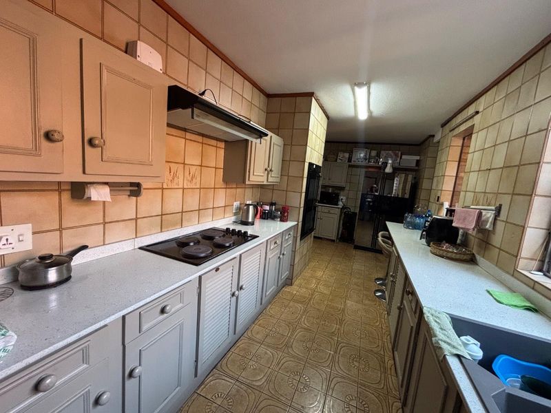 A functional galley-style kitchen featuring built-in cabinetry, an electric hob with extractor, and a double sink, currently showing dated finishes throughout.