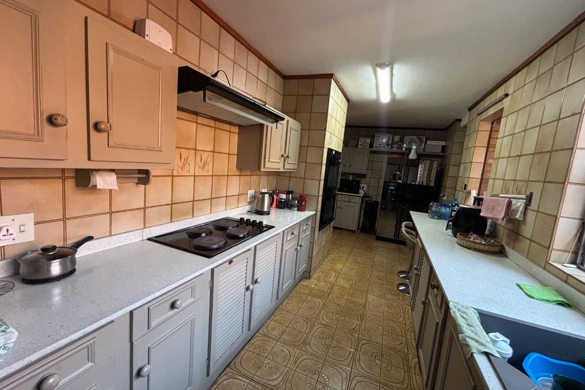 A functional galley-style kitchen featuring built-in cabinetry, an electric hob with extractor, and a double sink, currently showing dated finishes throughout.