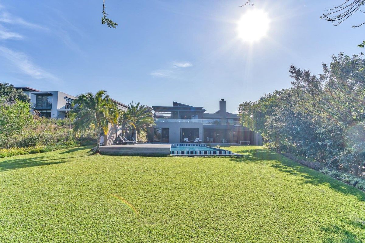 Rear view of a modern luxury residence featuring a swimming pool, timber deck, and expansive landscaped garden.