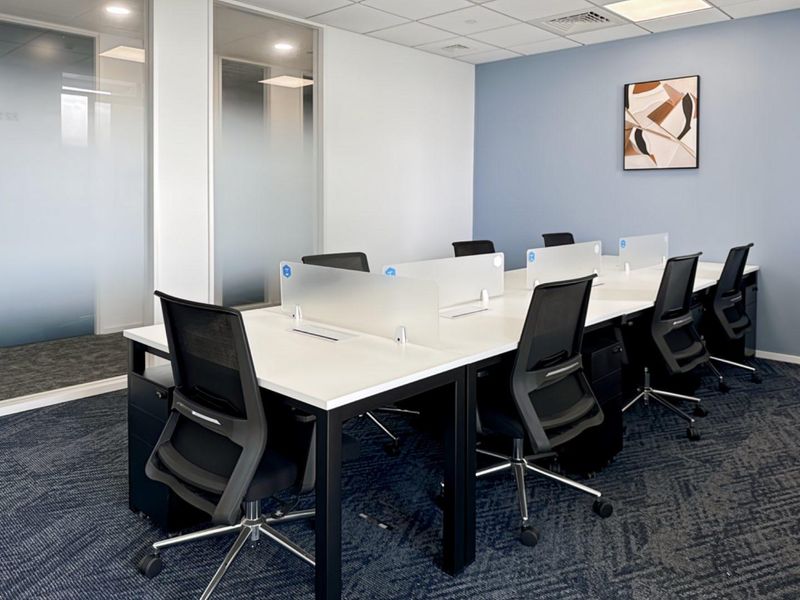Modern office workspace featuring glass partitions, suspended ceiling with recessed lighting, and professional carpet flooring in a clean, well-maintained environment.
