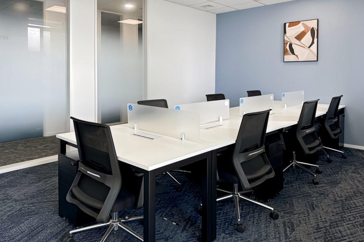 Modern office workspace featuring glass partitions, suspended ceiling with recessed lighting, and professional carpet flooring in a clean, well-maintained environment.