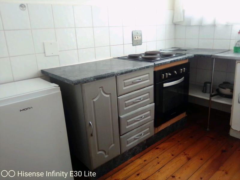 A compact kitchen featuring built-in cabinetry, a laminate countertop, an electric hob, and an oven with a tiled backsplash and timber flooring.