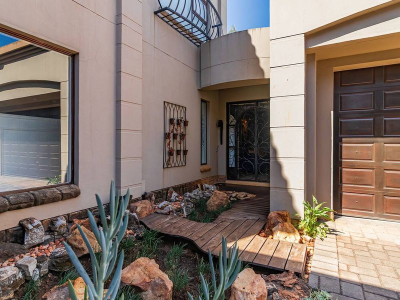 Front entrance featuring a decorative wrought iron security gate, a wooden walkway over a rock garden, and a modern sectional garage door.