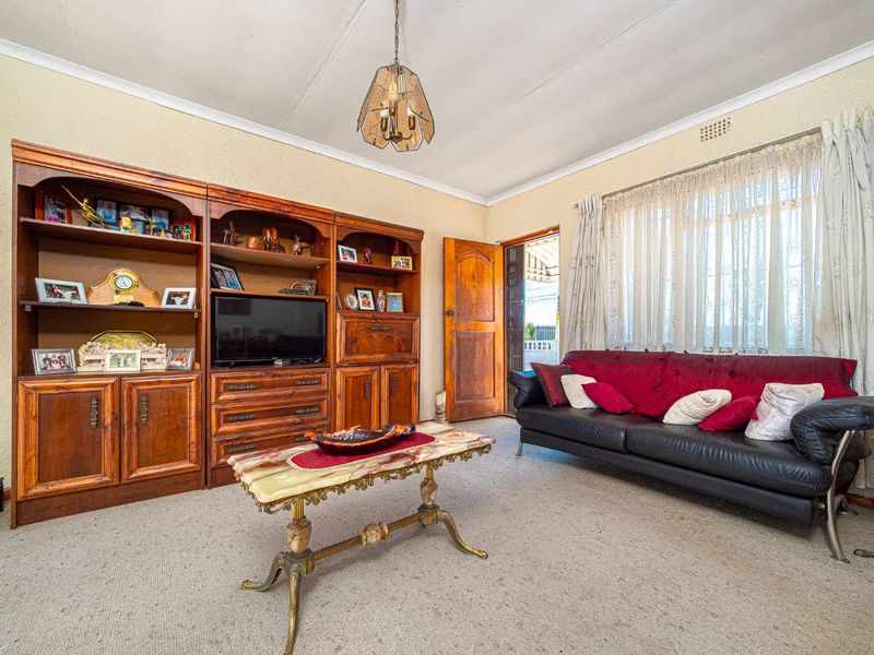 A dated living room featuring carpet flooring, coved cornicing, and a timber door leading to the exterior.