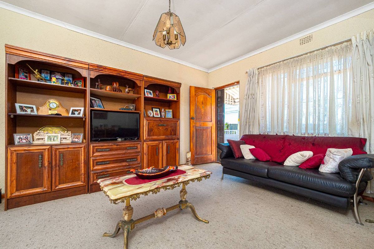 A dated living room featuring carpet flooring, coved cornicing, and a timber door leading to the exterior.