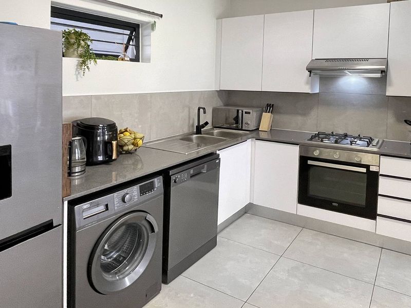 Modern kitchen featuring white cabinetry, stone countertops, integrated gas hob, oven, extractor fan, and tiled finishes with space for under-counter appliances.