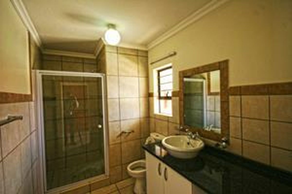 A functional bathroom featuring a shower enclosure, vanity with granite countertop, vessel sink, and tiled finishes throughout.